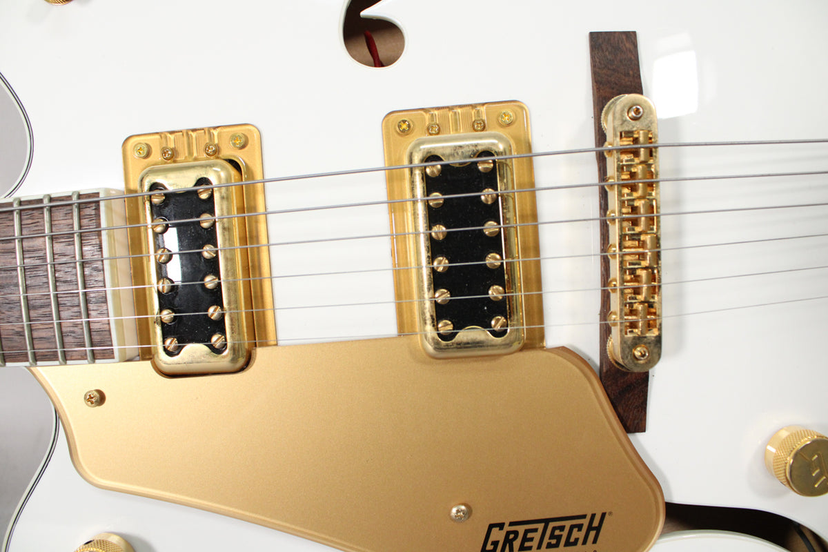 Close-up of the white guitar body, showing two gold humbucker pickups, a gold bridge, and a gold pickguard with light wear.