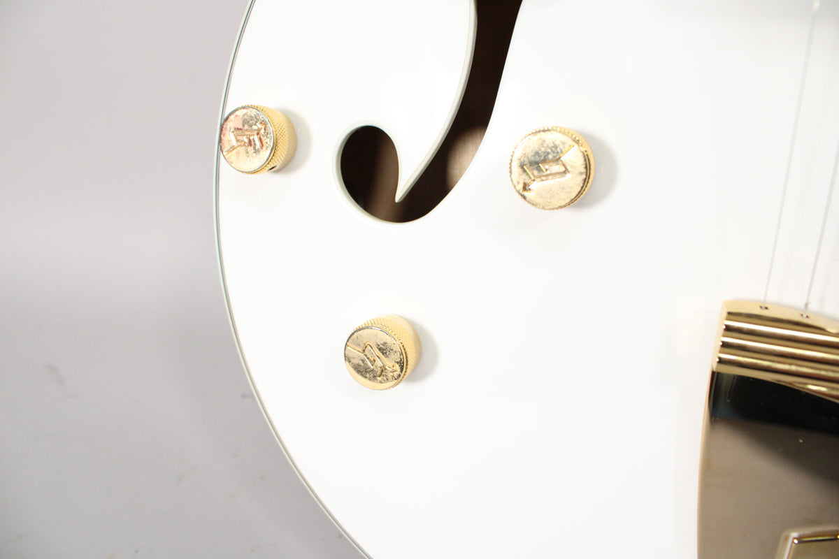 Close-up of the white hollow body, showing three gold control knobs with lightning bolt inserts and a gold bridge.