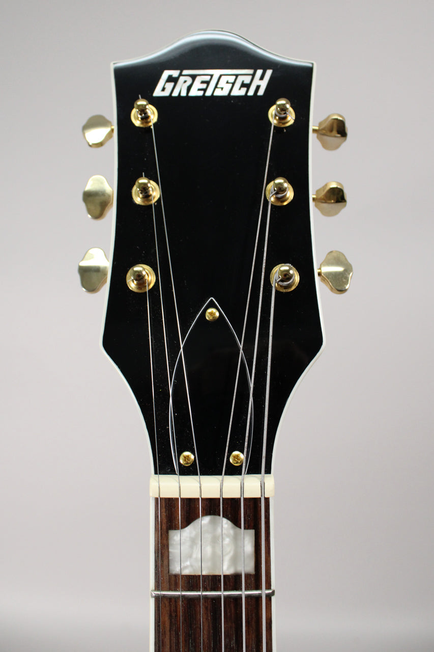 The black headstock with white binding and gold tuners is centered, showing the top of the fretboard with a mother-of-pearl inlay.