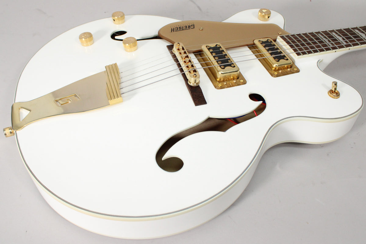 The white hollow body guitar is angled, showing its gold hardware, f-holes, and the upper part of the fretboard.