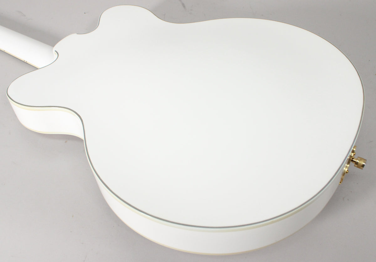 The back of a white hollow body guitar with cream binding, showing the neck joint and a gold strap button.