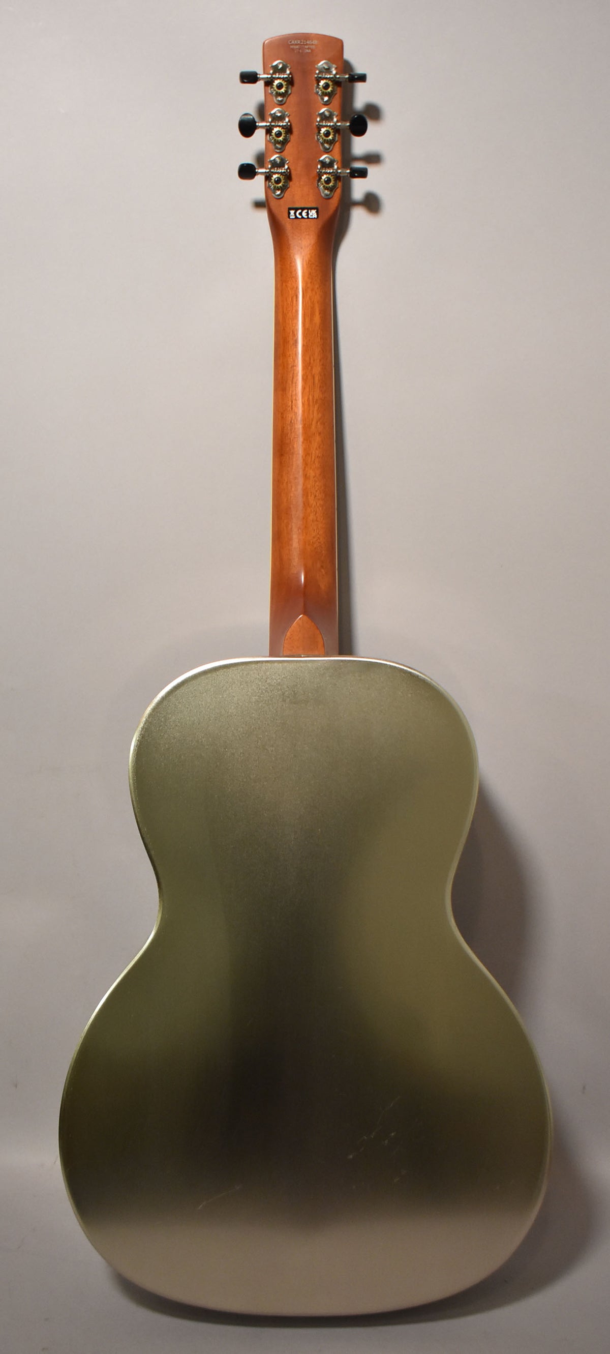 The back of the resonator guitar, showing its matte gold steel body with light scratches, a glossy brown neck, and six chrome tuners with black buttons.