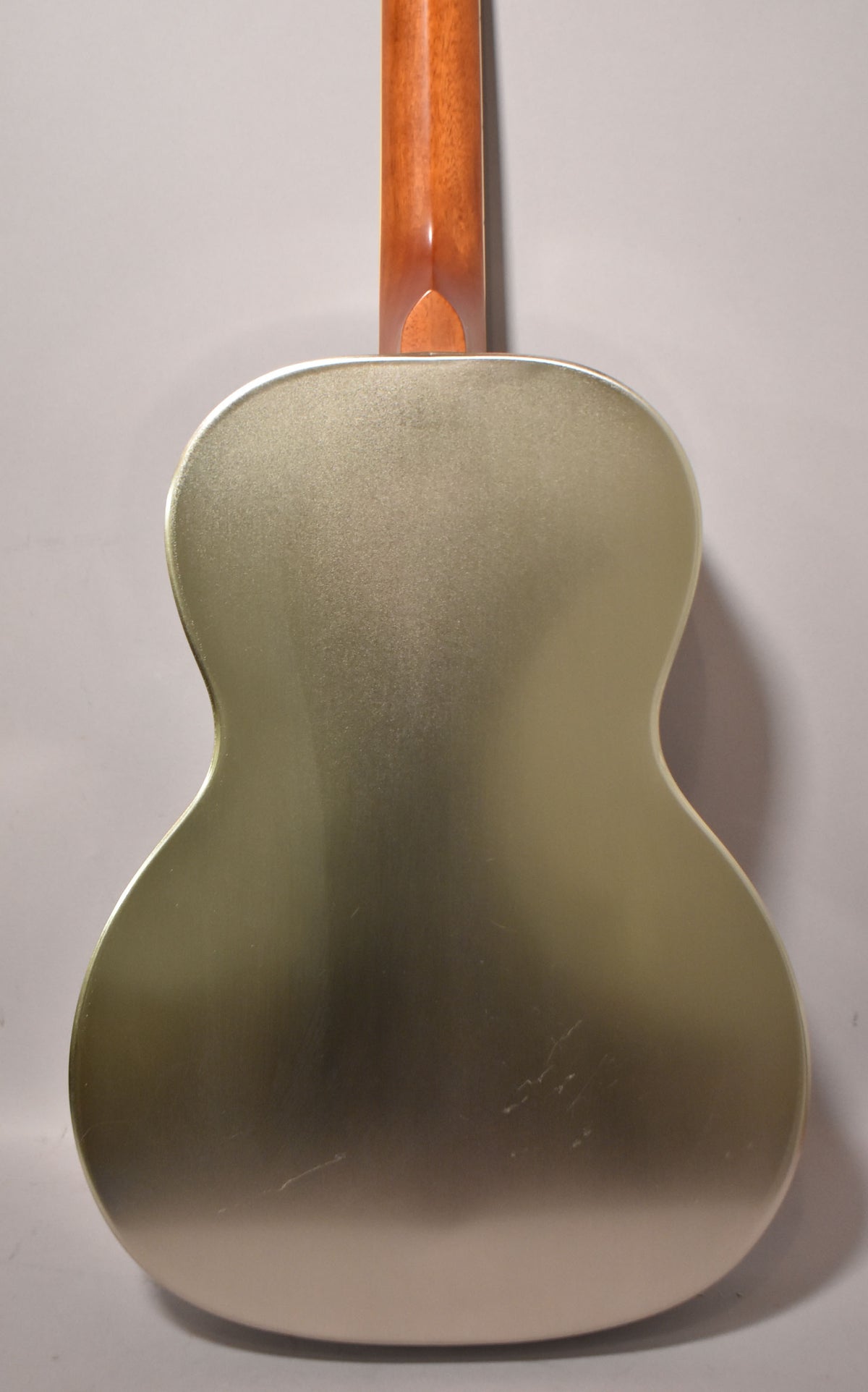 The back of a gold-colored resonator guitar with a light brown neck, showing some light scratches and scuffs on the body.