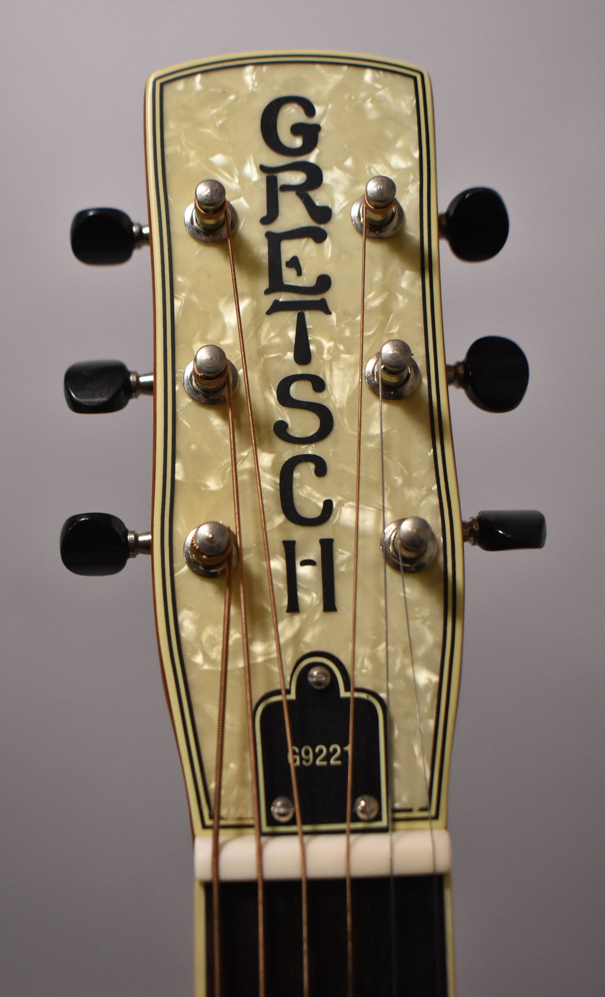 The headstock, angled slightly, features a pearloid finish with black tuning pegs and a black truss rod cover.