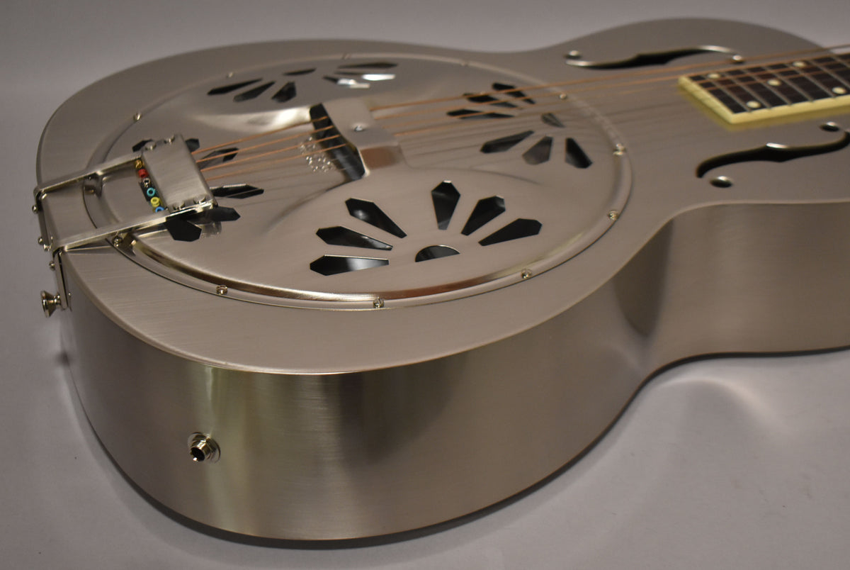 The brushed nickel resonator guitar is angled from the lower bout, showing the tailpiece with colored string ends and the output jack.