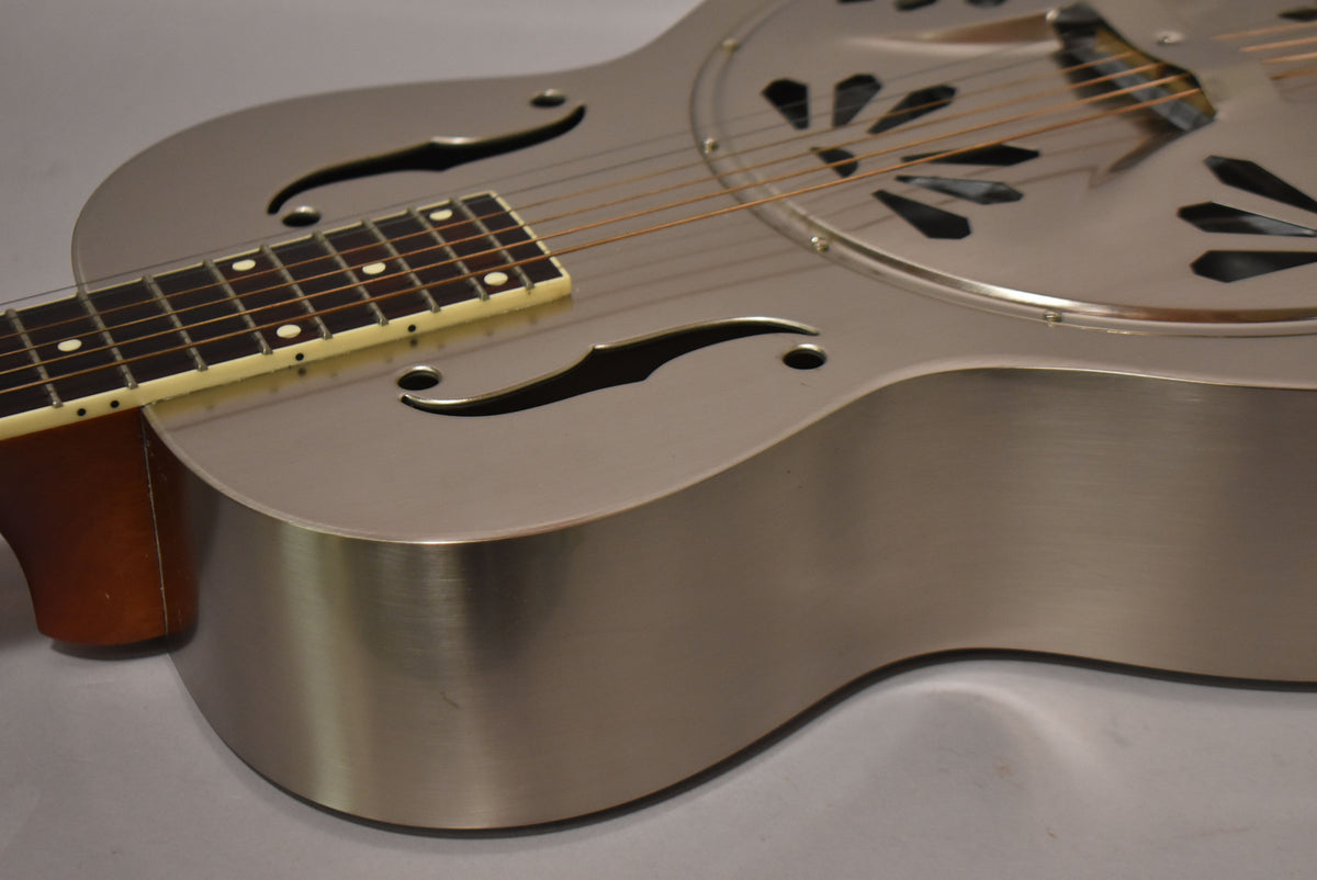 Upper body of a brushed steel resonator guitar with f-holes, a dark fretboard with white dot inlays, and a light binding.