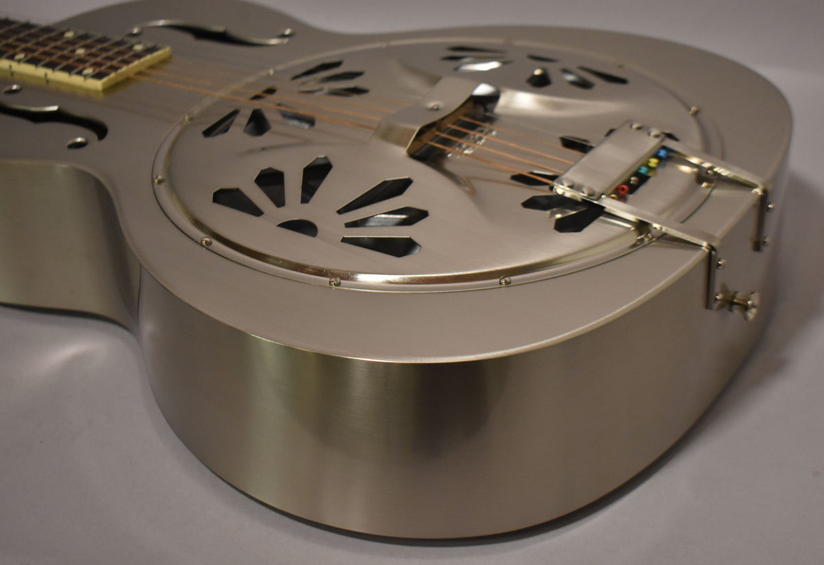 Close-up of the lower body of a brushed nickel resonator guitar, showing the patterned sound holes and tailpiece with colored string ends.
