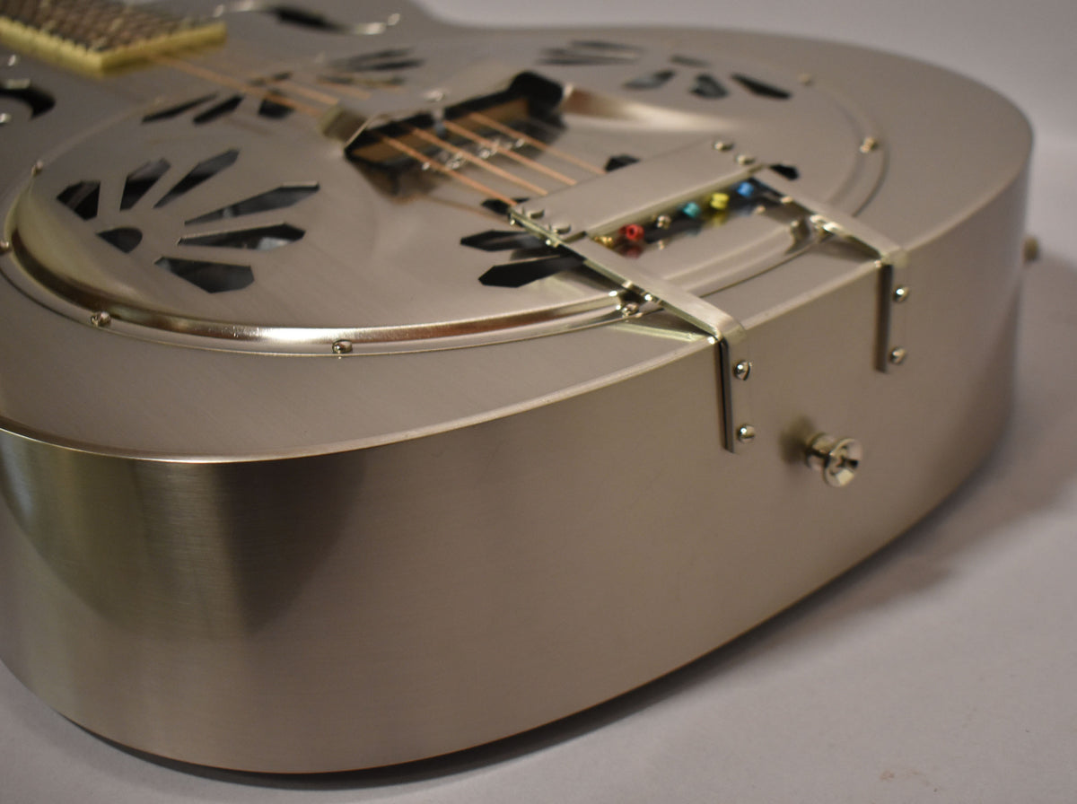 Close-up of the lower bout of a brushed nickel resonator guitar, showing the tailpiece, f-holes, and strap button.