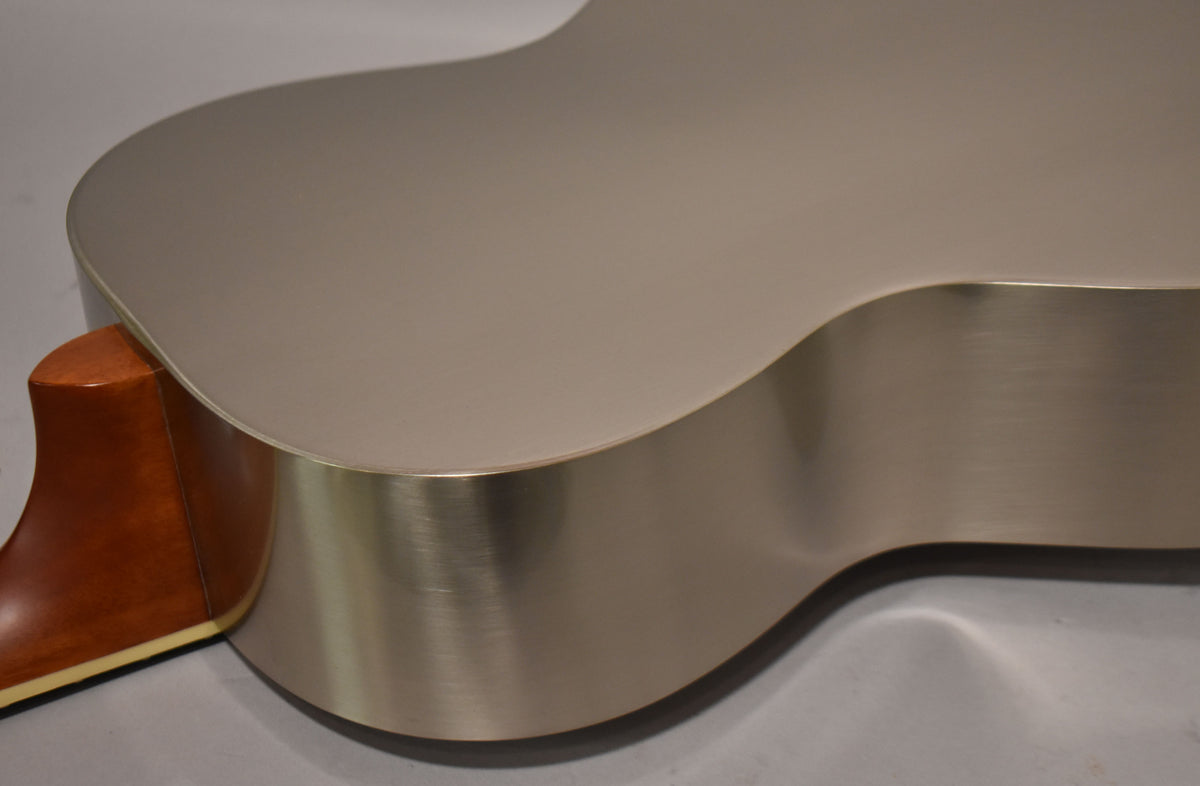 The guitar's brushed steel body and top are visible from the lower bout, with the light brown neck heel joining the body.
