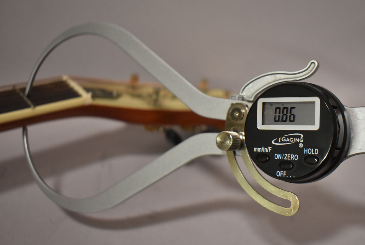 A digital caliper measures the guitar's nut width at 0.86, with the fretboard and headstock visible in the background.