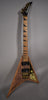 Full-length view of a V-shaped guitar with a natural wood body, gold hardware, black humbuckers, and black sharkfin inlays.