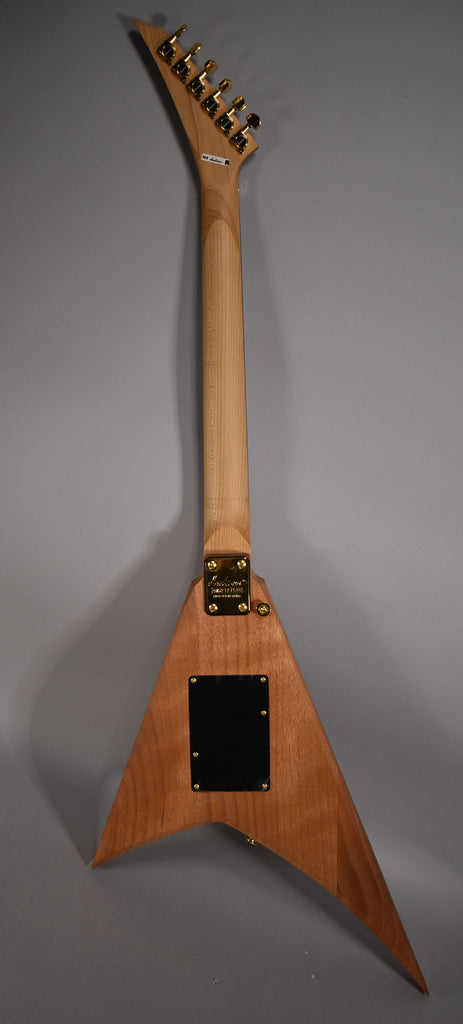 The back of a natural wood V-shaped guitar with a light-colored neck, gold tuners, and a gold neck plate.