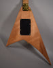 The back of a V-shaped guitar with a light brown wood grain finish, gold neck plate, and black control cavity cover.