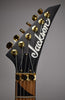 Close-up of the matte black headstock with gold tuners and locking nut, showing the dark wood fretboard with triangular inlays.