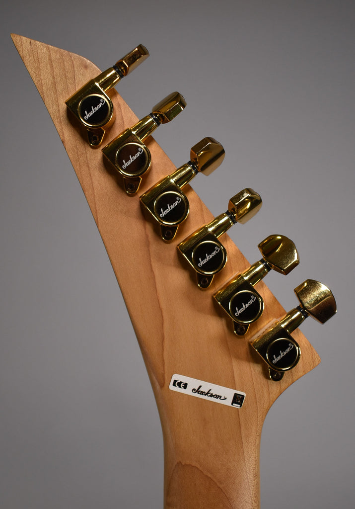 Close-up of the guitar's light wood headstock and neck, angled right, showing six gold-plated tuning machines.