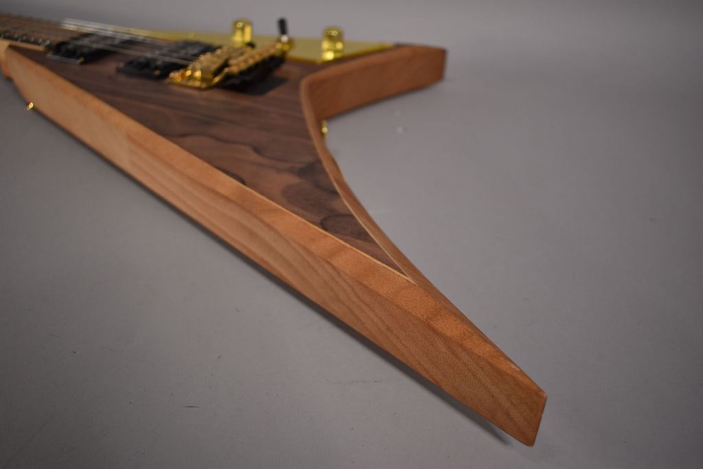 Close-up of the V-shaped body's lower wing, showing the dark ziricote top and lighter wood sides, with gold hardware visible.
