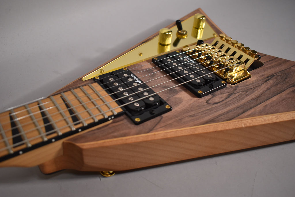 Close-up of the guitar body, showing the dark wood grain, gold hardware, black humbuckers, and light wood neck.