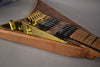 Close-up of the guitar's body, showing the natural wood grain, gold hardware, black humbuckers, and a reflective gold control plate.