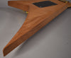 The back of a natural wood Rhoads-style guitar body, angled from the lower bout to the upper wing, with a black control plate.