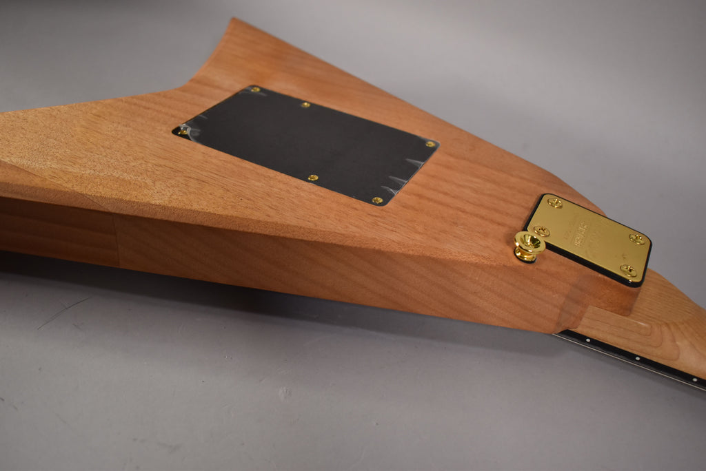The back of a natural wood guitar body, showing a black control plate and a gold neck plate with a strap button.
