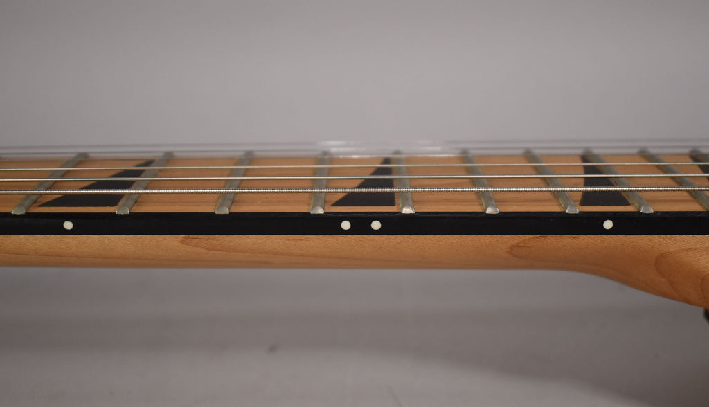 Close-up of the guitar's light brown maple neck and dark fretboard with black sharkfin inlays and white side dots.