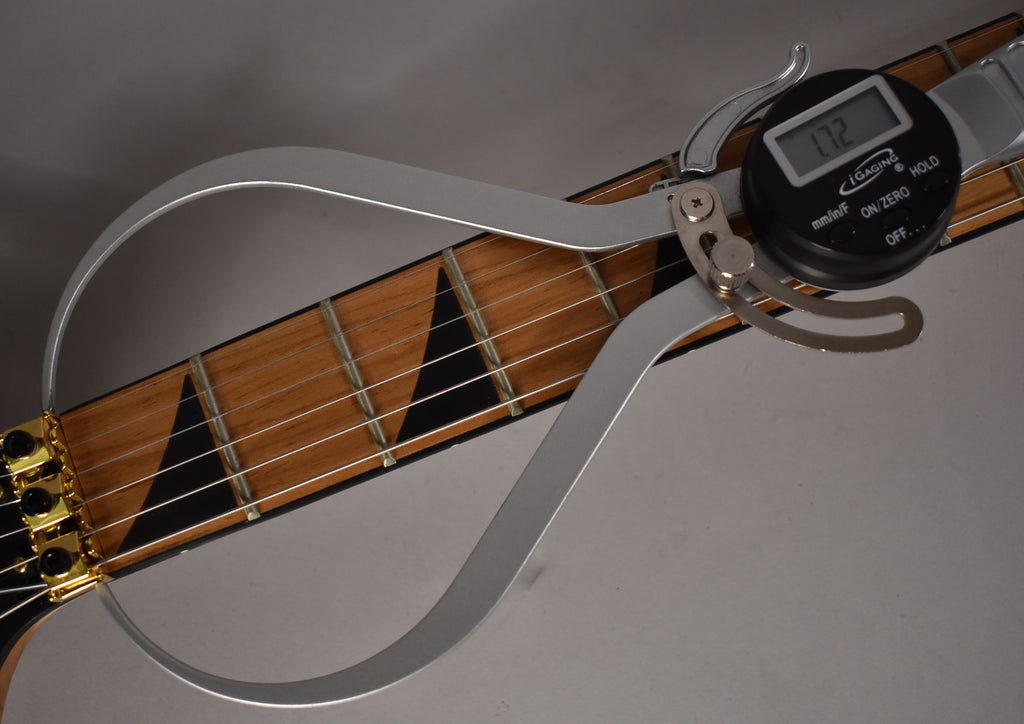 A digital fret rocker measures the guitar's frets, showing a reading of 1.72 over the light brown fretboard with black sharkfin inlays.