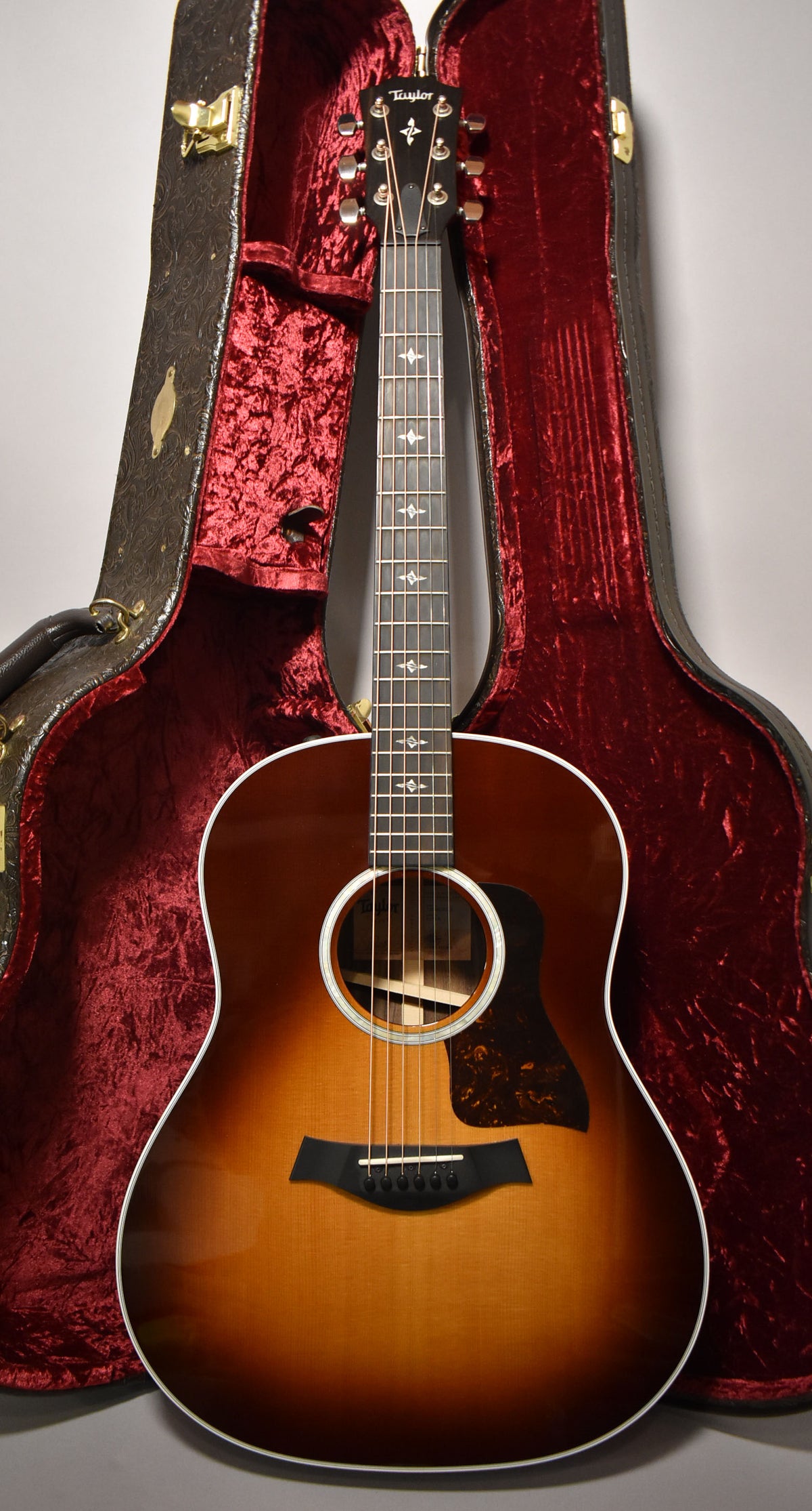 Full-front view of a sunburst acoustic guitar with a tortoiseshell pickguard, standing in its open, red-lined hard case.