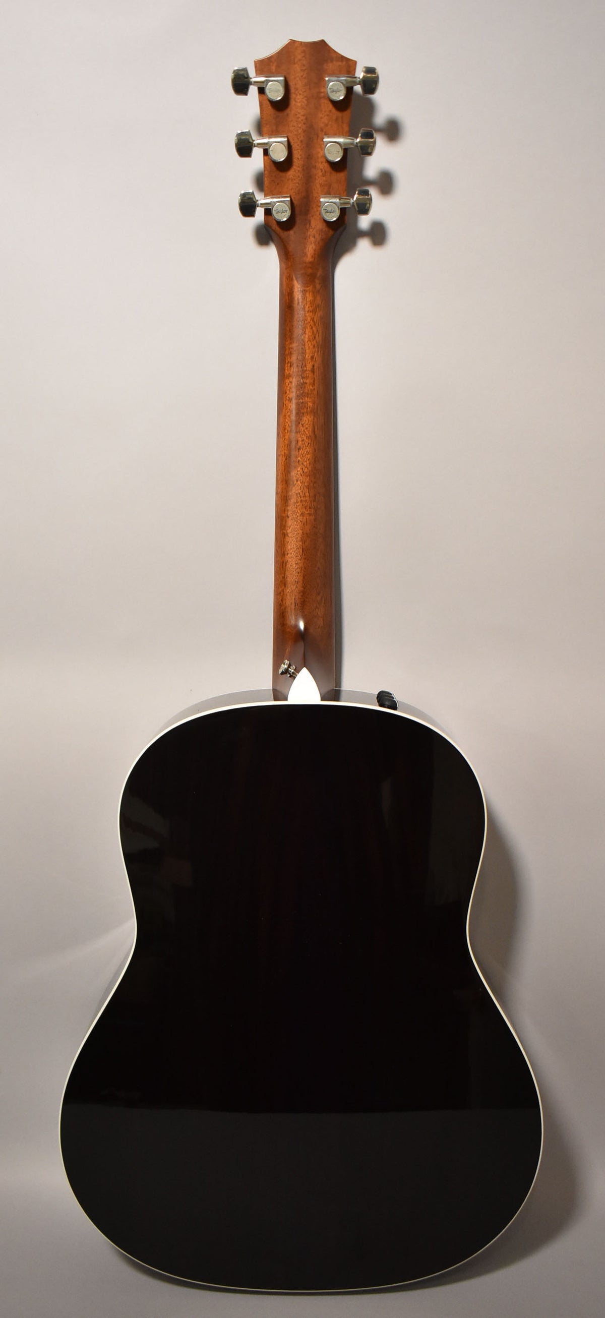 The back of a guitar with a dark, glossy body, a light brown neck, and six silver tuning pegs on the headstock.