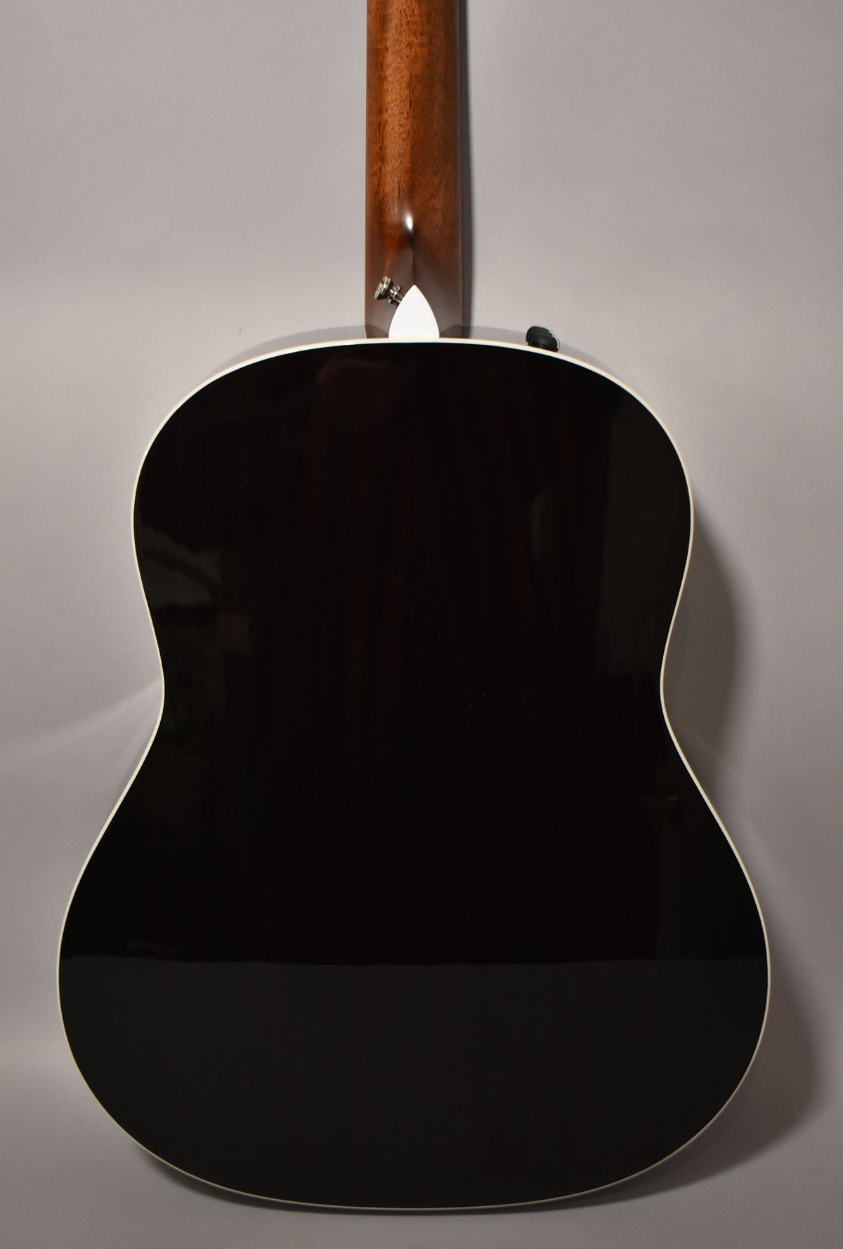 The guitar's glossy dark brown back and sides are framed from the rear, with a light wood neck and white binding visible.