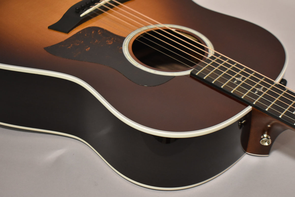 The sunburst acoustic guitar is angled from the upper left, showing the lower bout, soundhole, pickguard, and fretboard.