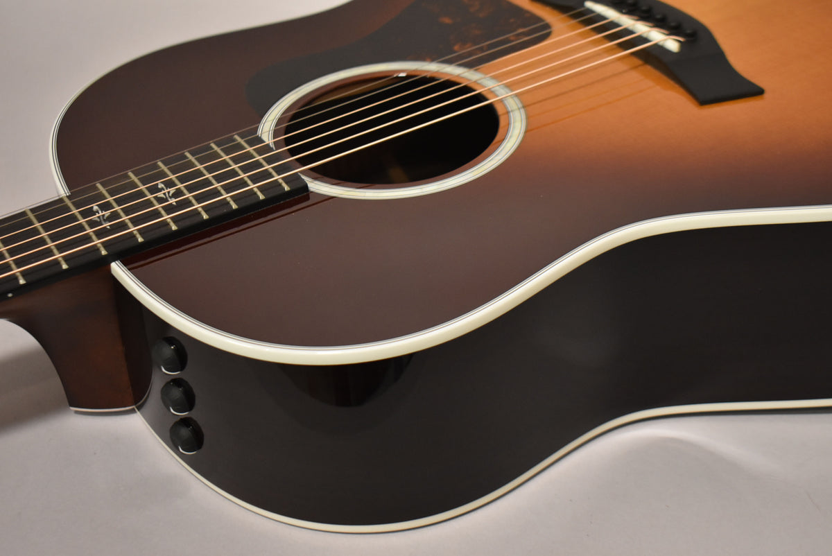 The sunburst acoustic guitar is angled from the lower bout, showing three black control knobs on the upper side.