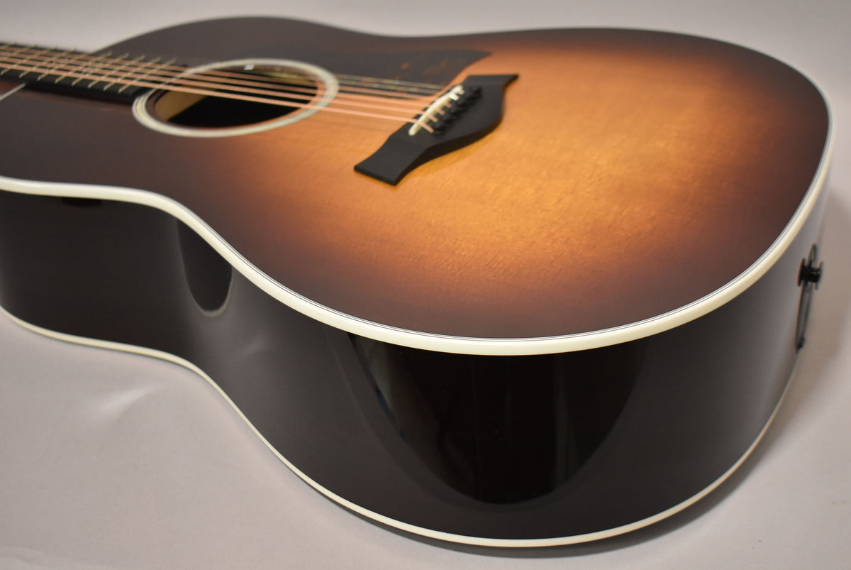 The guitar's sunburst top fades from dark brown to amber, with a black bridge and white binding, viewed from the upper bout.