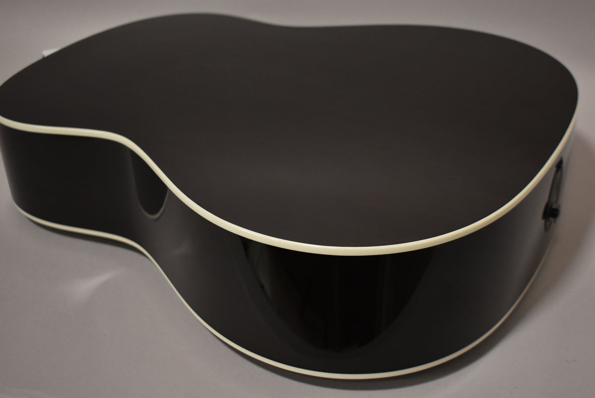 The guitar's dark sunburst back and sides are visible from above, with cream binding and an endpin jack on the lower bout.