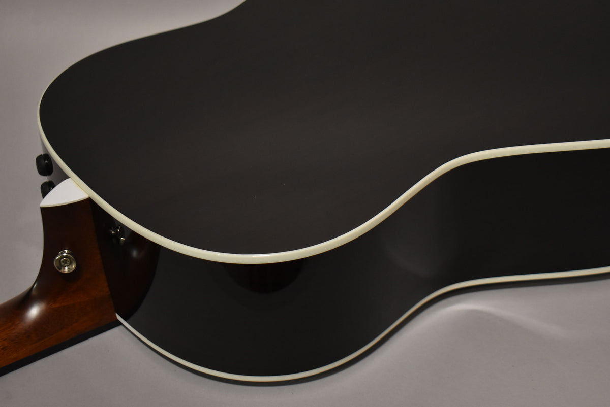 The guitar's matte black back and glossy black sides are visible, with cream binding and a mahogany neck heel.