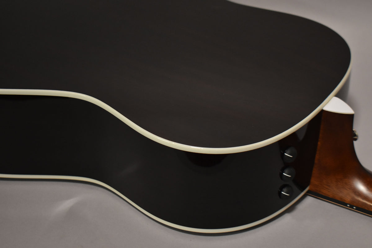The guitar's dark sunburst back and side are framed, showing three black control knobs and cream binding along the edges.