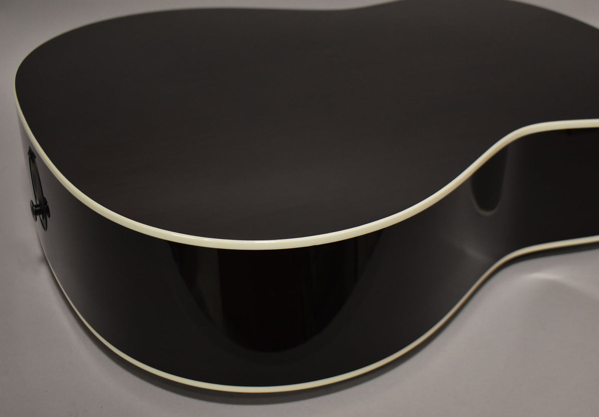 The guitar's glossy black body and sides are visible from above, with cream binding and a visible strap button.