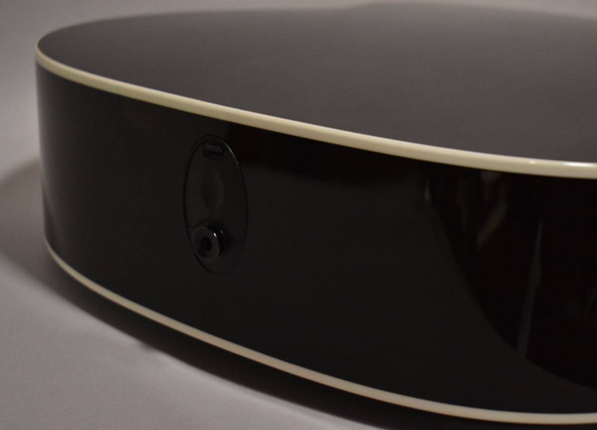 Close-up of the guitar's glossy black lower bout, showing the output jack and two small control knobs, framed by cream binding.