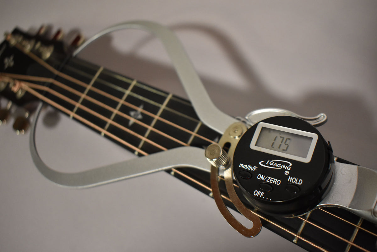 A digital caliper measures the guitar's nut width at 1.75 inches, resting on the dark fretboard and strings.