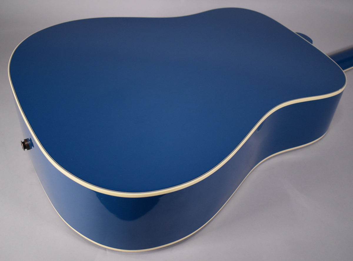 The back and side of the acoustic guitar's Big Sky Blue body are visible, with cream binding and a dark strap button on the lower bout.