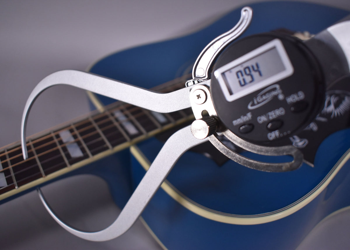 A digital caliper measures the Big Sky Blue guitar's body thickness at 0.94, with the fretboard and binding visible.