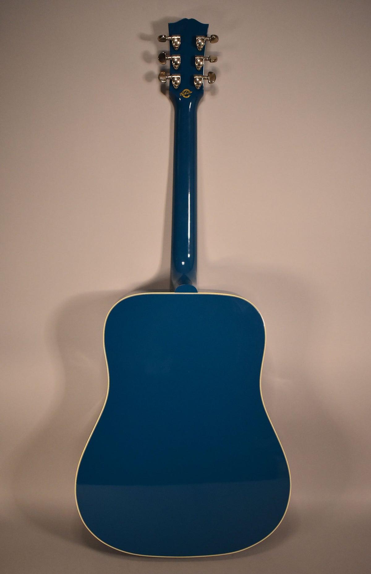 The full back of a glossy blue acoustic guitar is shown, with a matching headstock and gold tuning pegs.