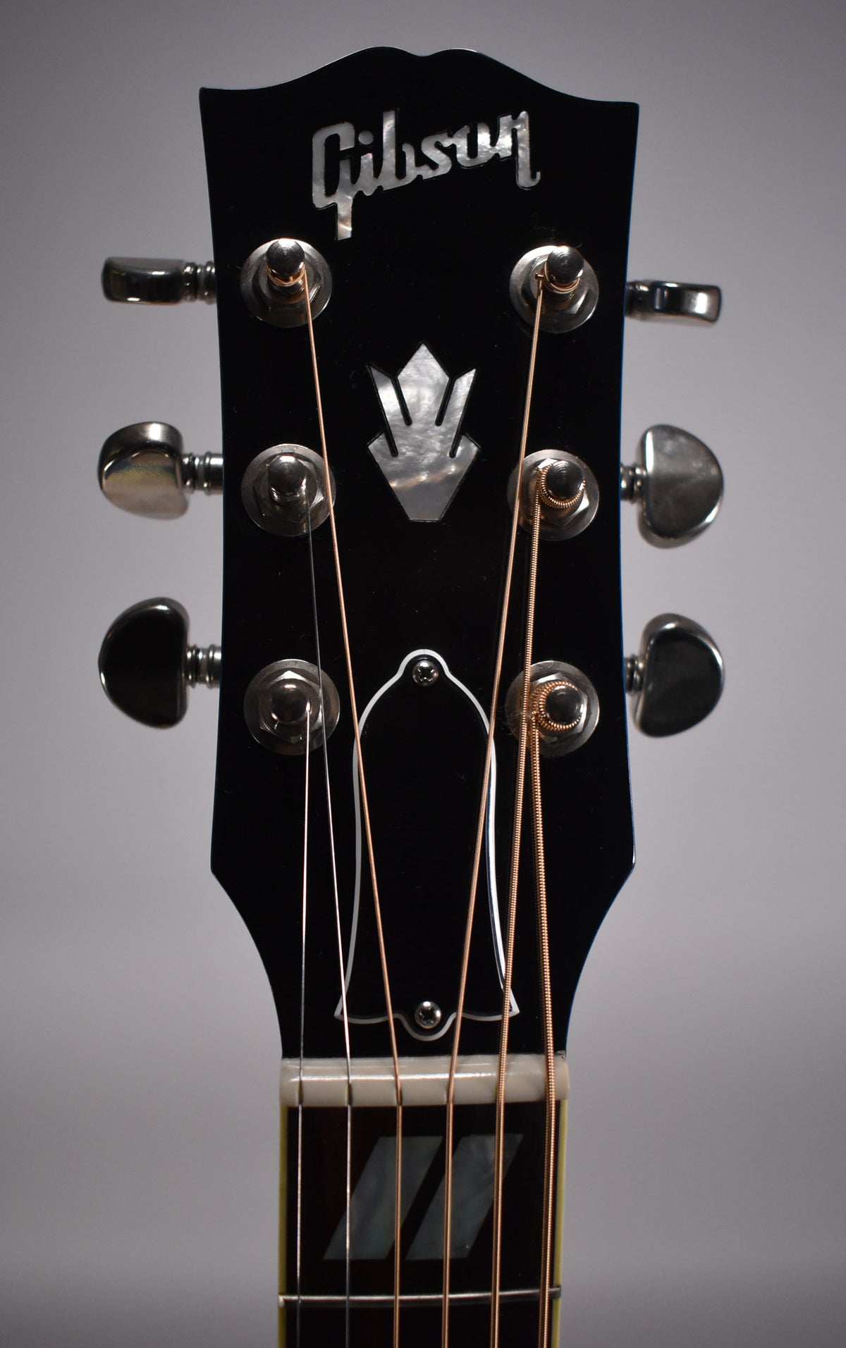 Close-up of the black headstock with mother-of-pearl inlay, chrome tuners, and a white nut, showing the top of the fretboard.