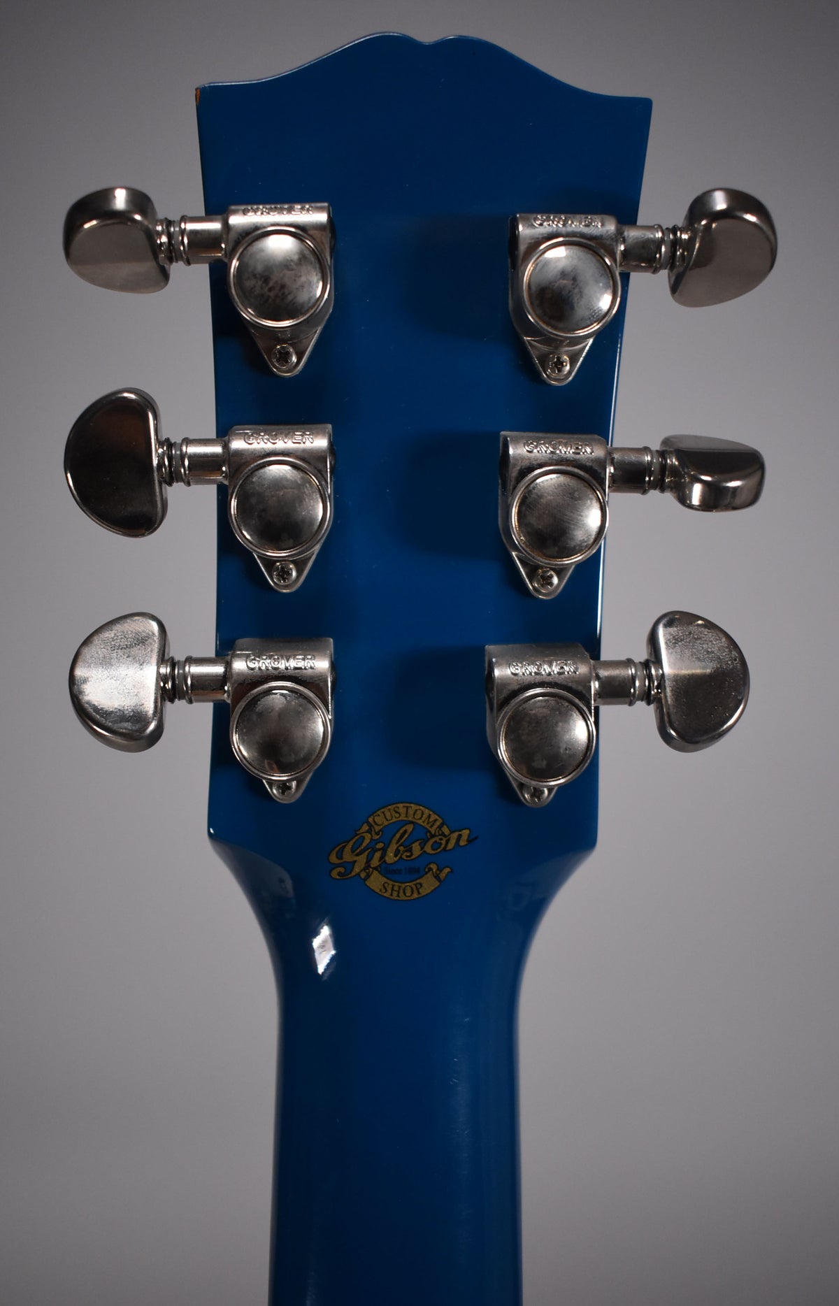 Rear view of the guitar's Big Sky Blue headstock and neck, showing six chrome tuners with light wear and a gold Custom Shop logo.