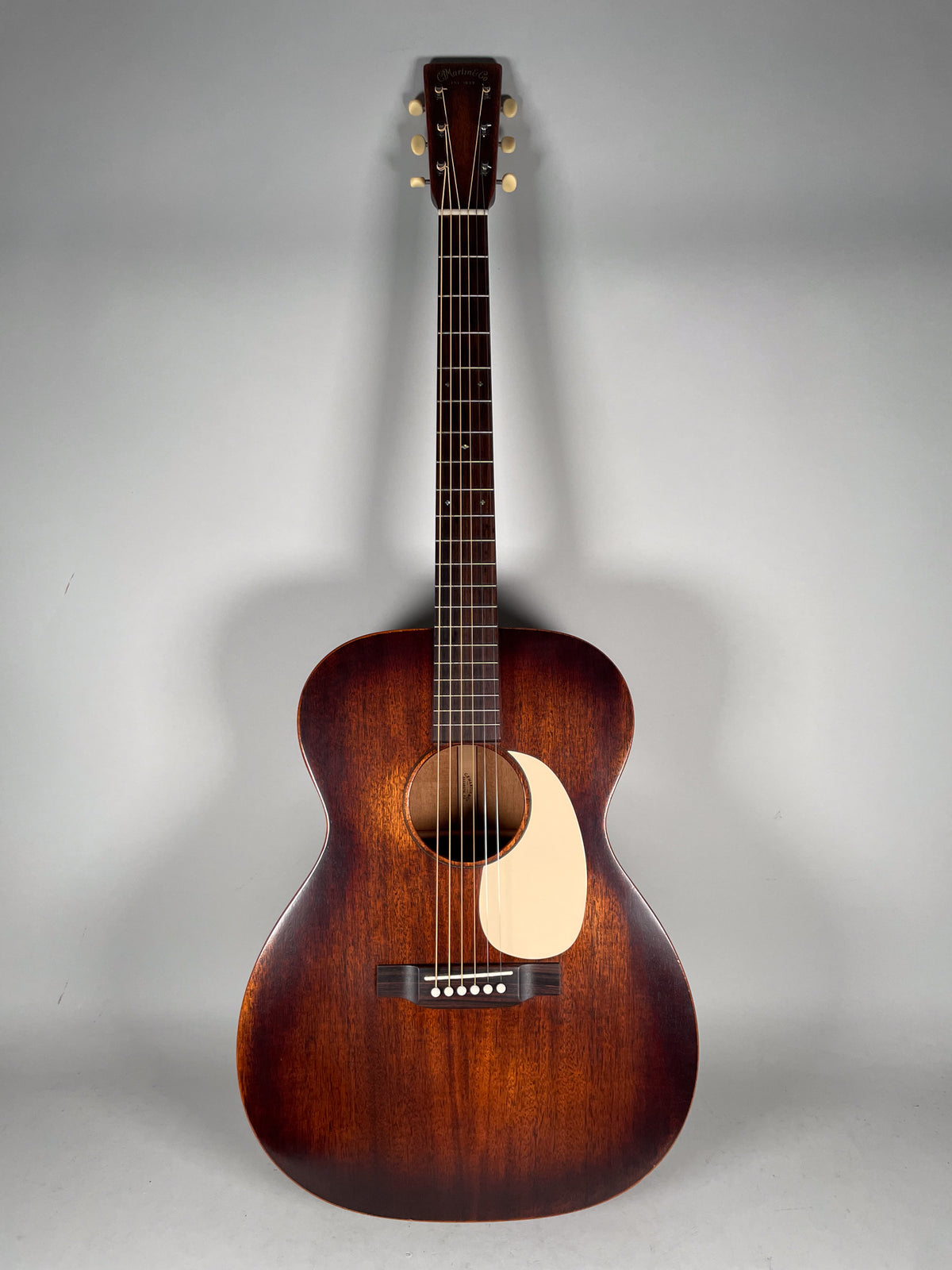Full-front view of a dark brown acoustic guitar with a matte finish, cream pickguard, and six white tuning pegs.