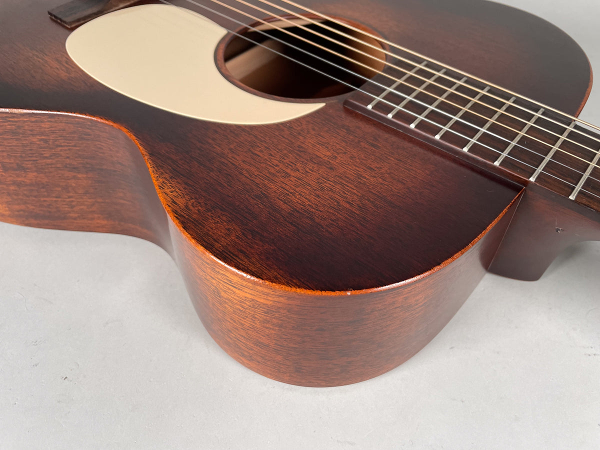 The dark brown acoustic guitar's lower bout and waist are visible, showing a light pickguard and distressed finish with worn edges.
