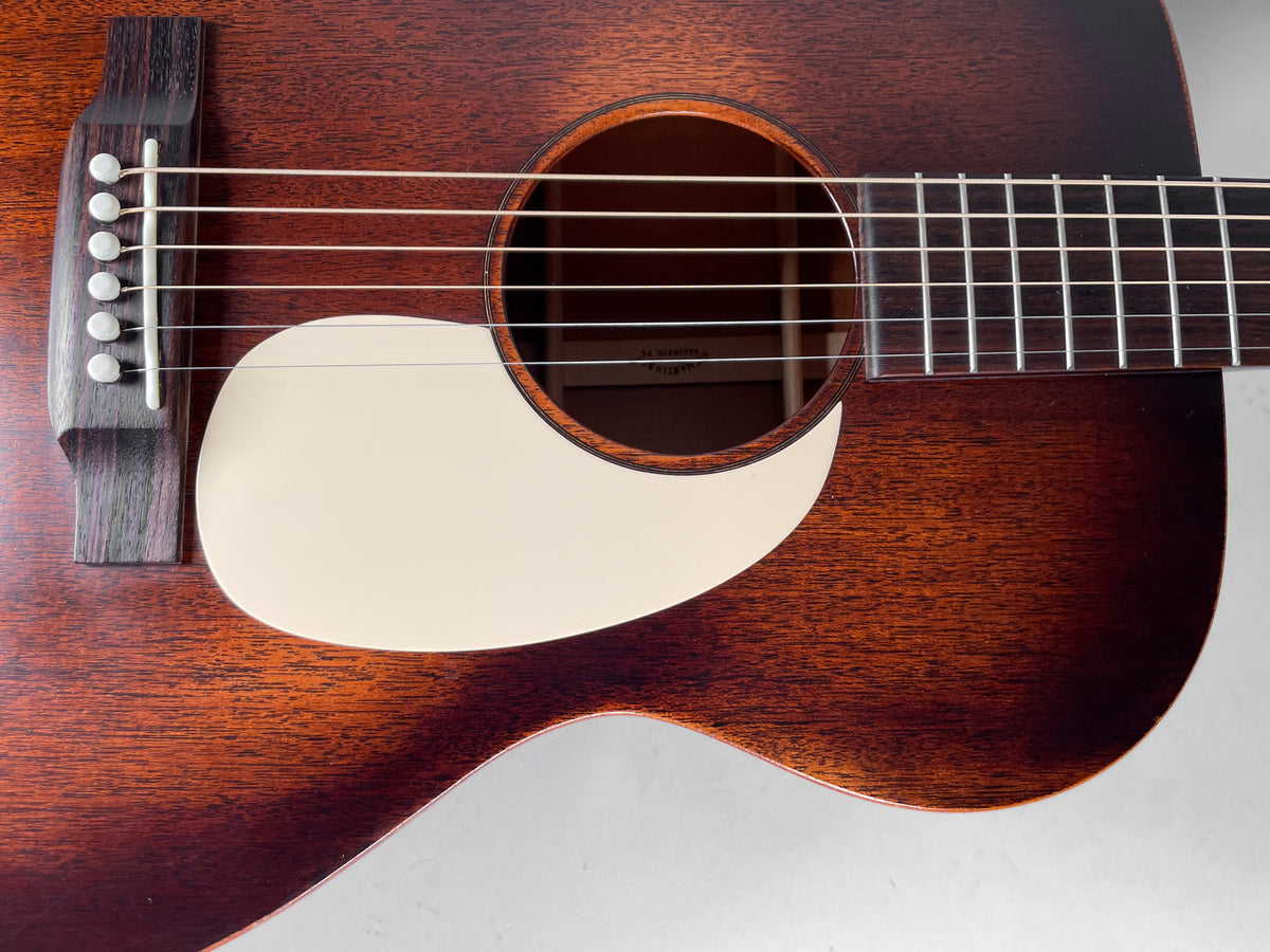 Close-up of the dark brown acoustic guitar's body, showing the soundhole, cream pickguard, bridge, and lower fretboard.