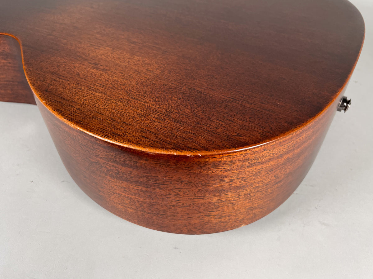 The lower bout and side of the dark brown acoustic guitar, showing a satin finish and a strap button on the bottom.