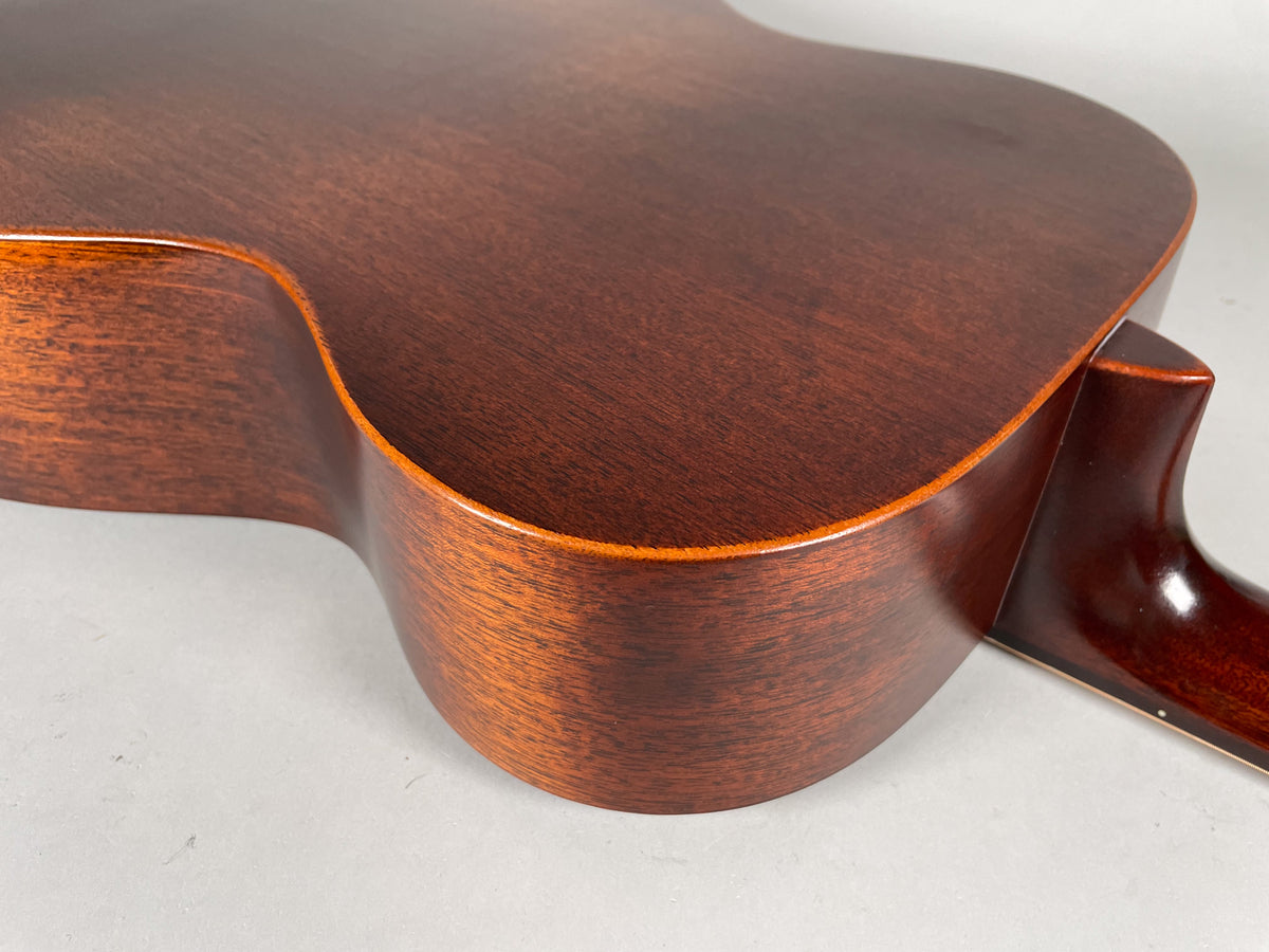 The lower bout and cutaway of a dark brown acoustic guitar, showing the satin finish and neck heel.