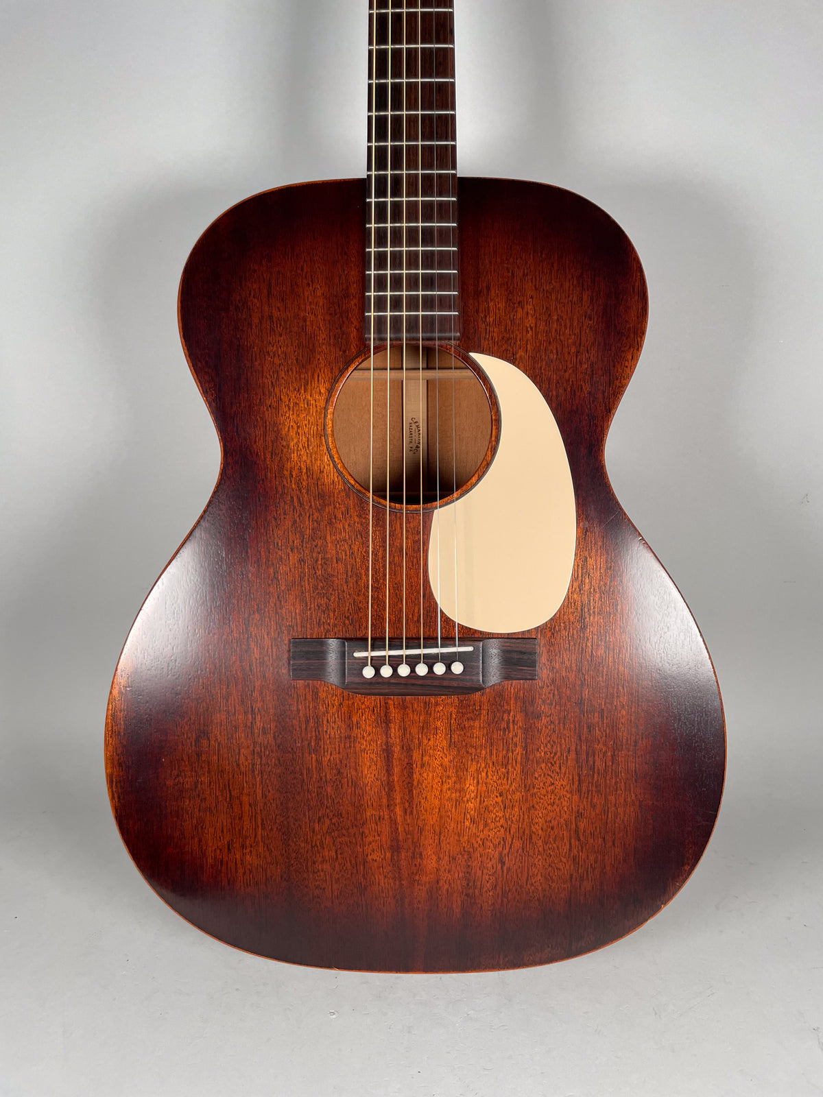 Full front view of a dark reddish-brown acoustic guitar with a light cream pickguard, showing the body, soundhole, and fretboard.