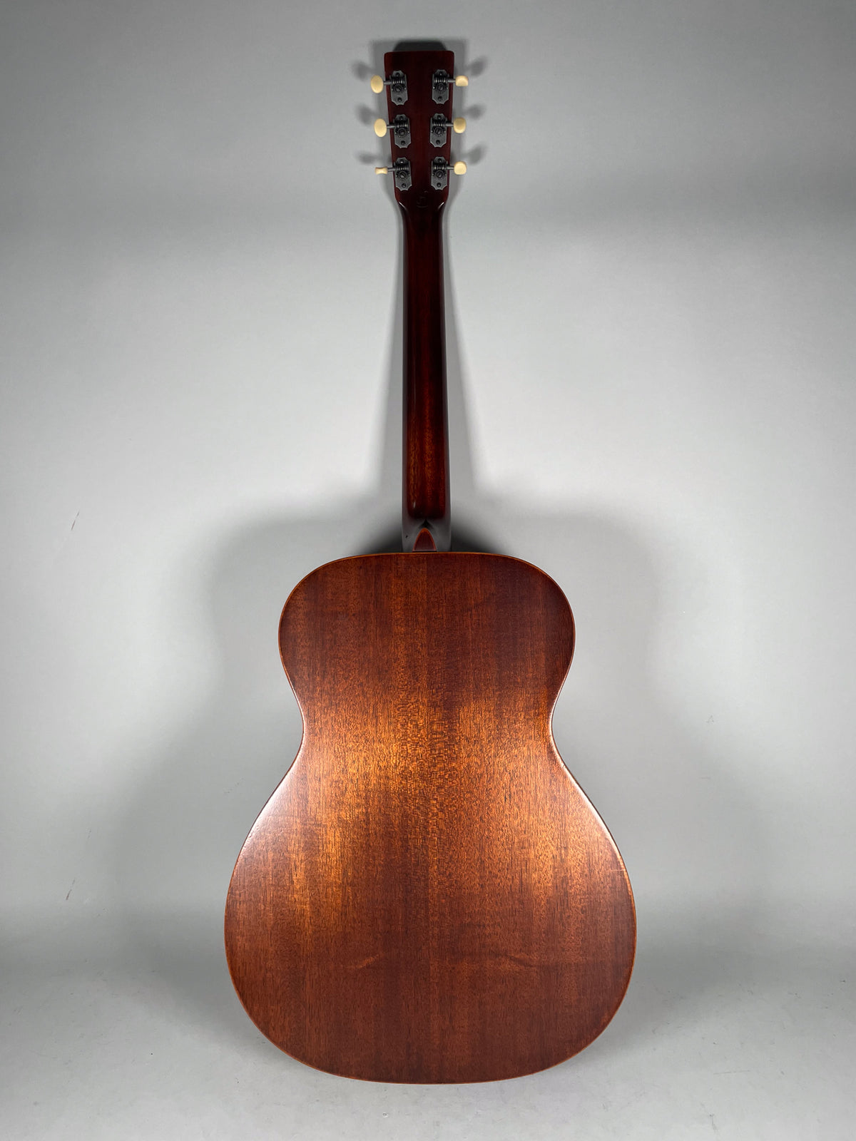 Full rear view of the dark reddish-brown acoustic guitar, showing the body's wood grain and six cream-colored tuning pegs.